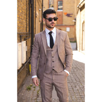 Man klädd i brun kostym och solglasögon på en gata.