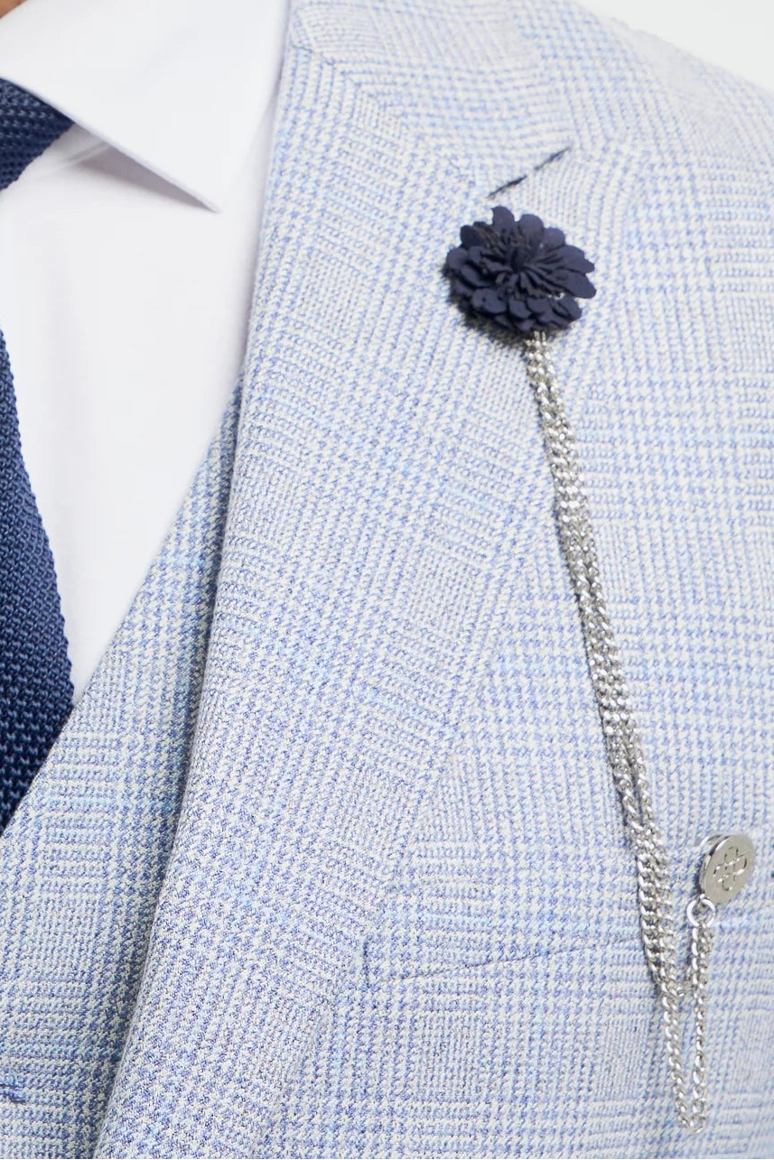 Man klädd i ljusgrå kostym med marinblå slips och blommig nål på vit bakgrund